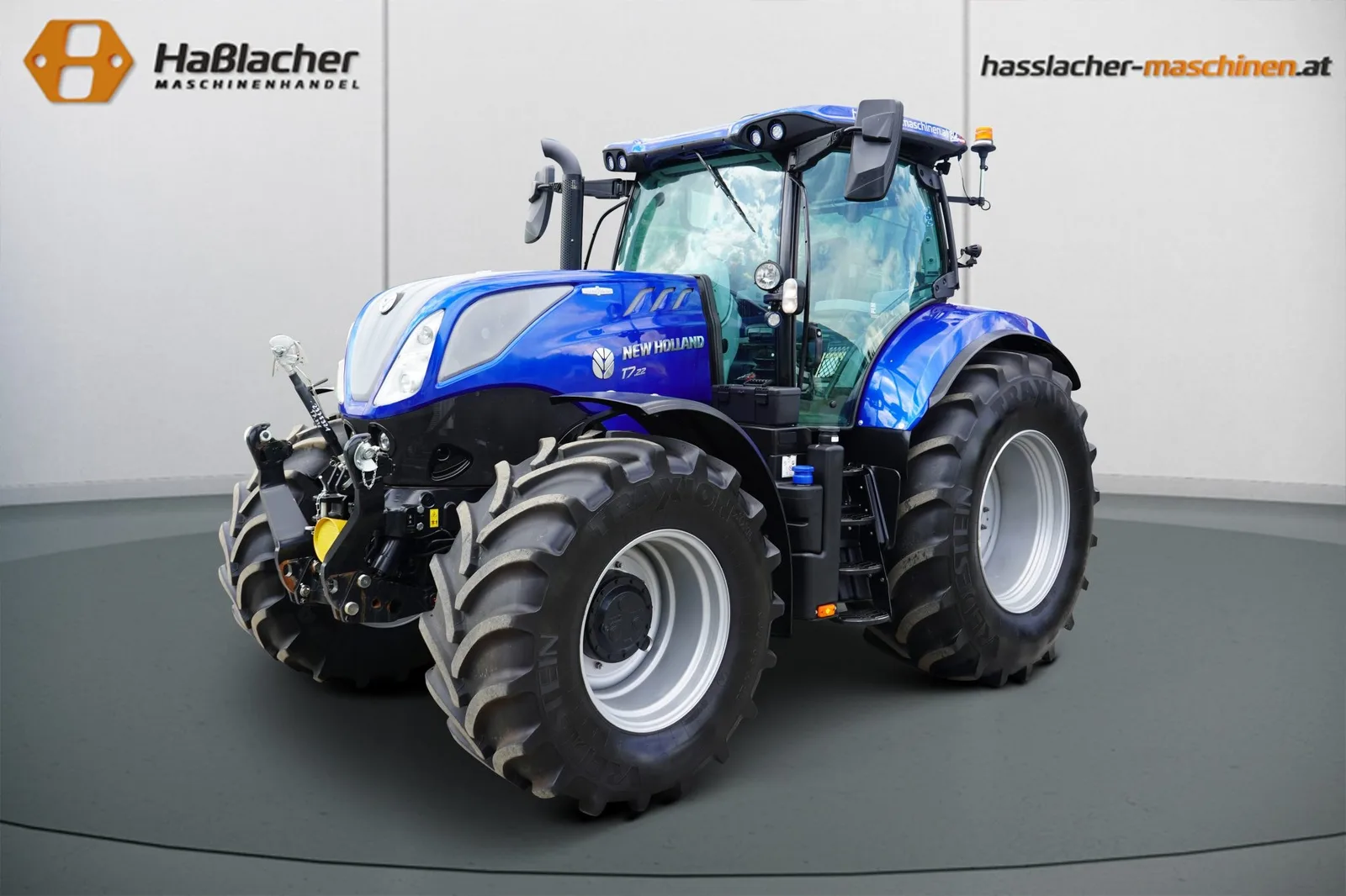 Dunkelblauer New Holland Traktor mit Fronthydraulik vor der Haßlacher-Fotowand