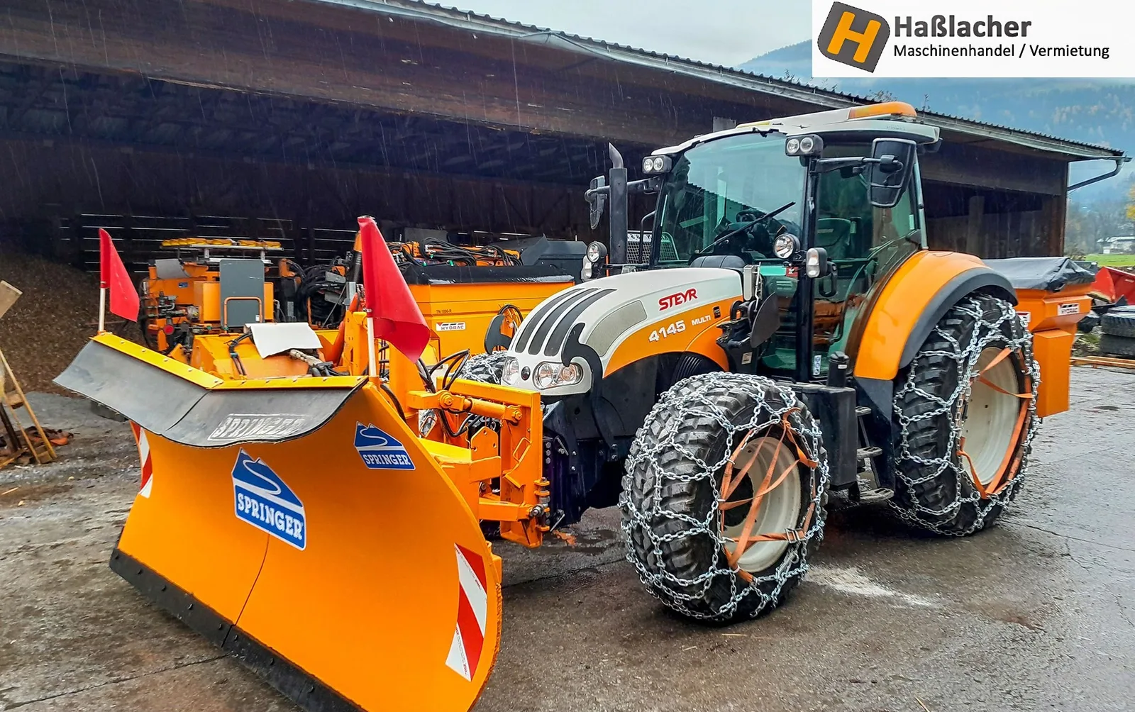 Steyr Traktor mit Netzketten und orangem Springer Schneepflug vor einem Holzunterstand
