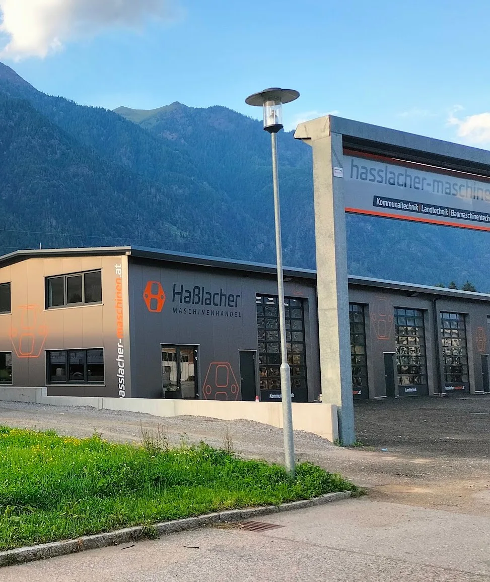 Halle von Haßlacher Maschinenhandel mit Logo und Firmenschild, dahinter die Berge des Drautals